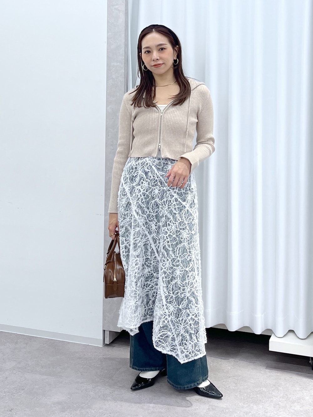 ベージュ系のニット/セーター、ブラウン系のハンドバッグ、ブルー系のデニムパンツを着用したレディースの冬コーディネートの2枚目の写真