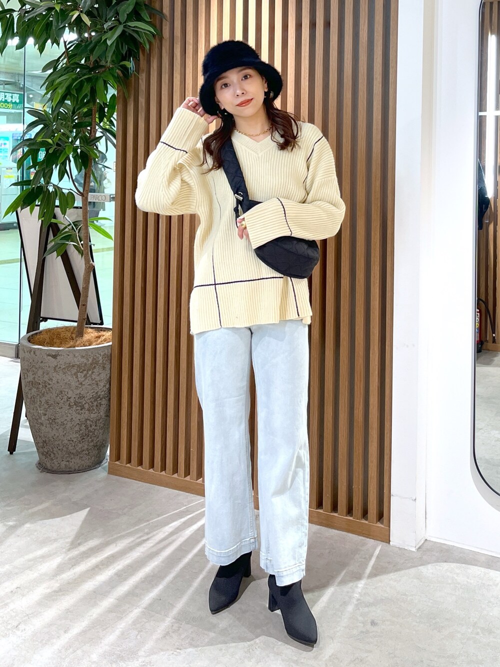 ブラック系のショルダーバッグ、ホワイト系のニット/セーター、ブルー系のデニムパンツを着用したレディースの冬コーディネートの3枚目の写真