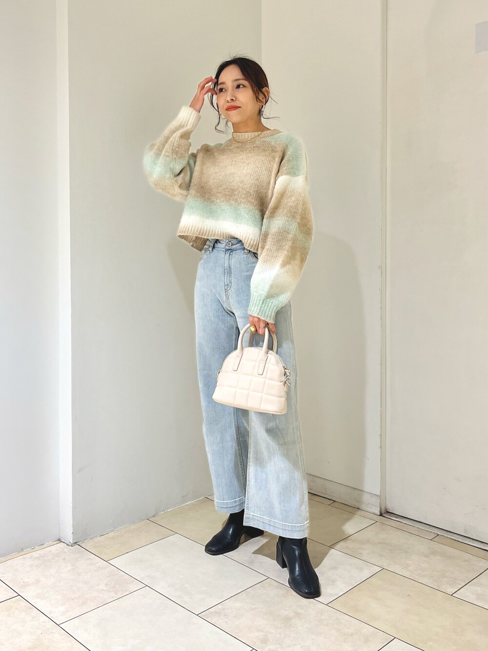 ホワイト系のデニムパンツ、グリーン系のニット/セーター、ホワイト系のハンドバッグを着用したレディースの冬コーディネートの2枚目の写真