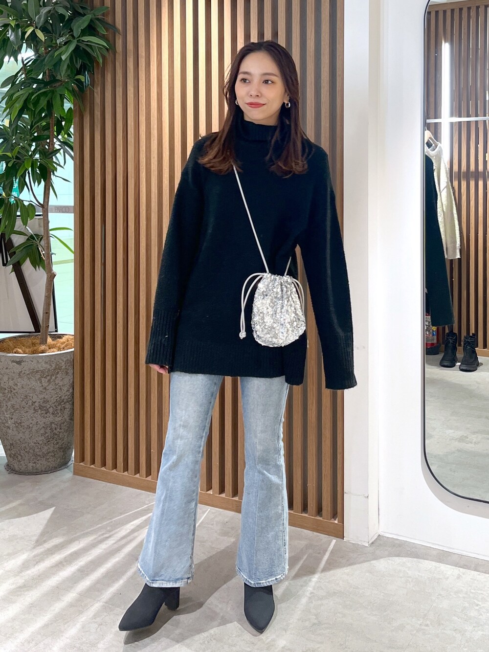 シルバー系のハンドバッグ、ブラック系のニット/セーター、ブルー系のデニムパンツを着用したレディースの冬コーディネートの5枚目の写真