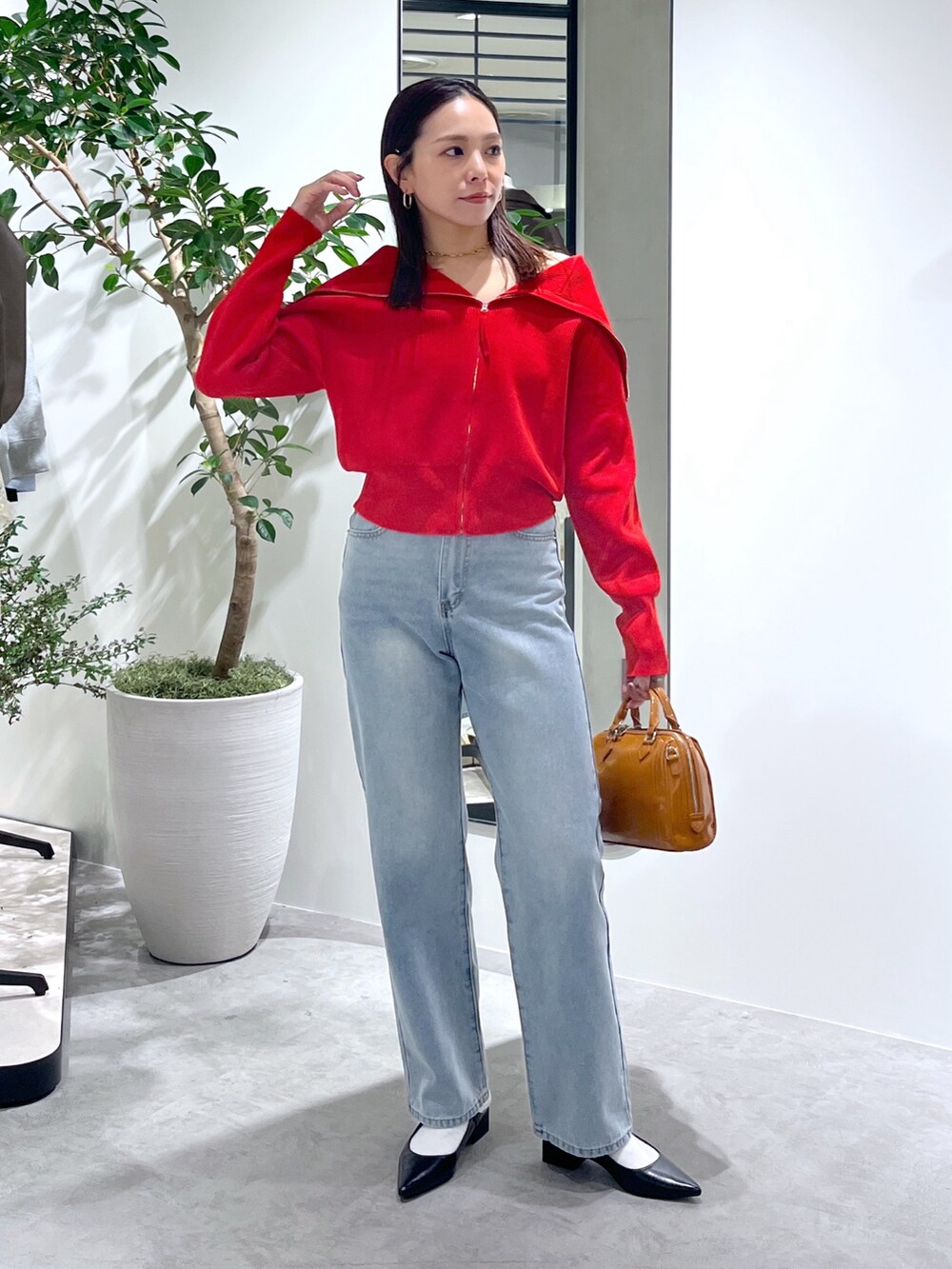 レッド系のニット/セーター、ブルー系のデニムパンツ、ベージュ系のショルダーバッグを着用したレディースの春コーディネートの3枚目の写真