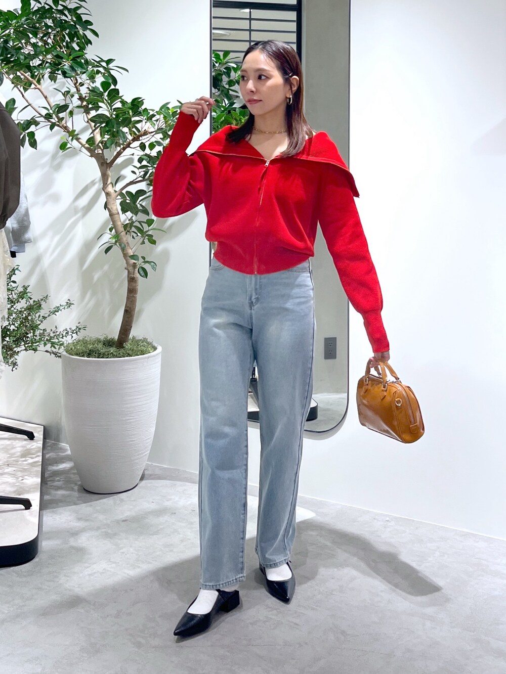 レッド系のニット/セーター、ブルー系のデニムパンツ、ベージュ系のショルダーバッグを着用したレディースの春コーディネートの6枚目の写真