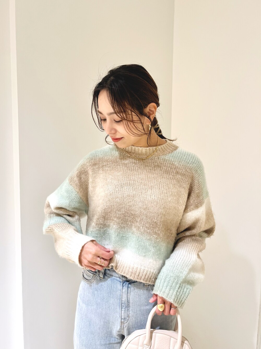 ホワイト系のデニムパンツ、グリーン系のニット/セーター、ホワイト系のハンドバッグを着用したレディースの冬コーディネートの4枚目の写真