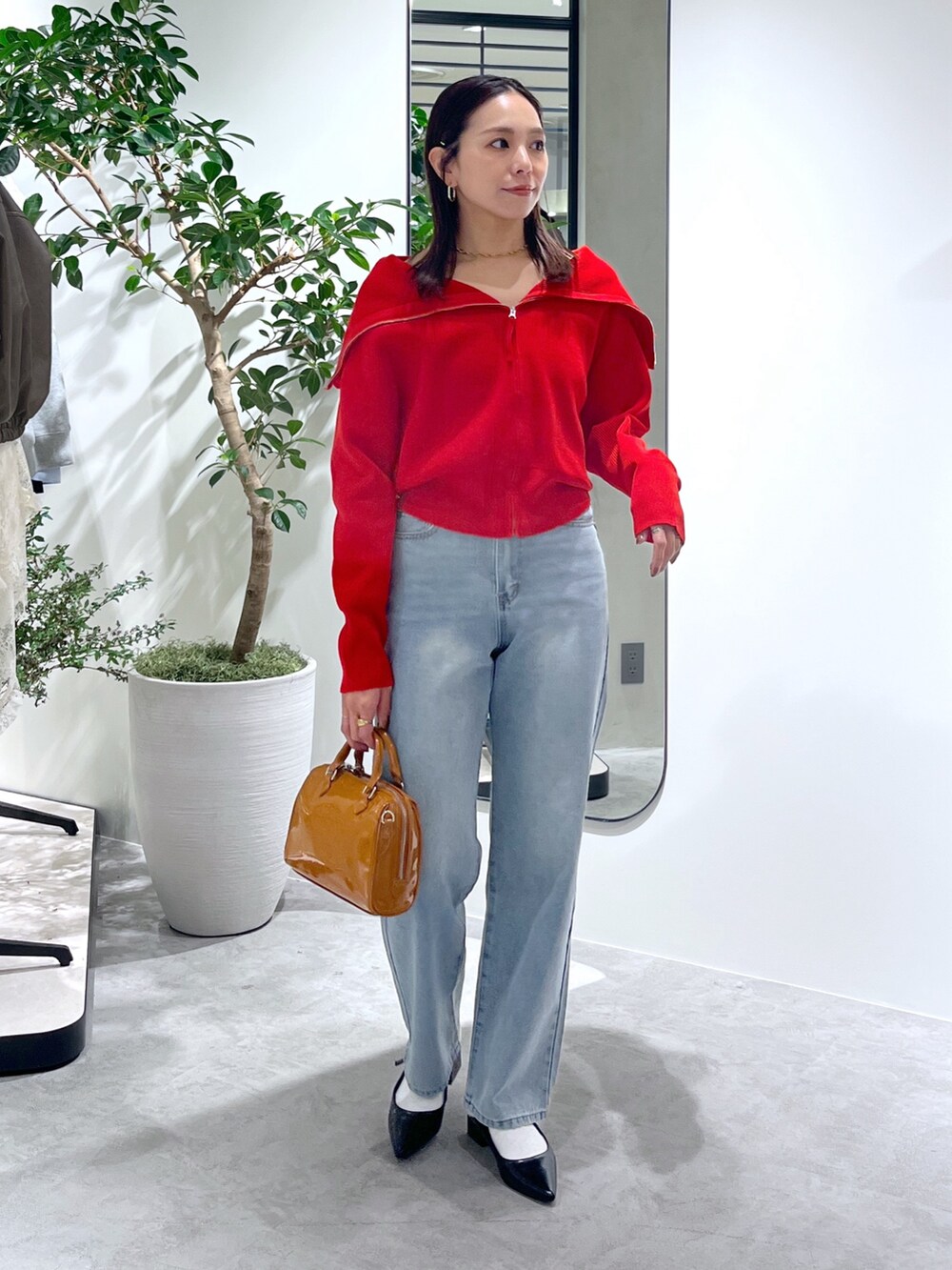 レッド系のニット/セーター、ブルー系のデニムパンツ、ベージュ系のショルダーバッグを着用したレディースの春コーディネートの4枚目の写真