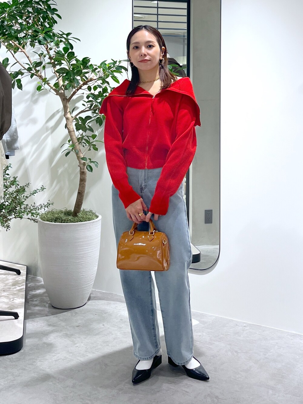 レッド系のニット/セーター、ブルー系のデニムパンツ、ベージュ系のショルダーバッグを着用したレディースの春コーディネートの2枚目の写真