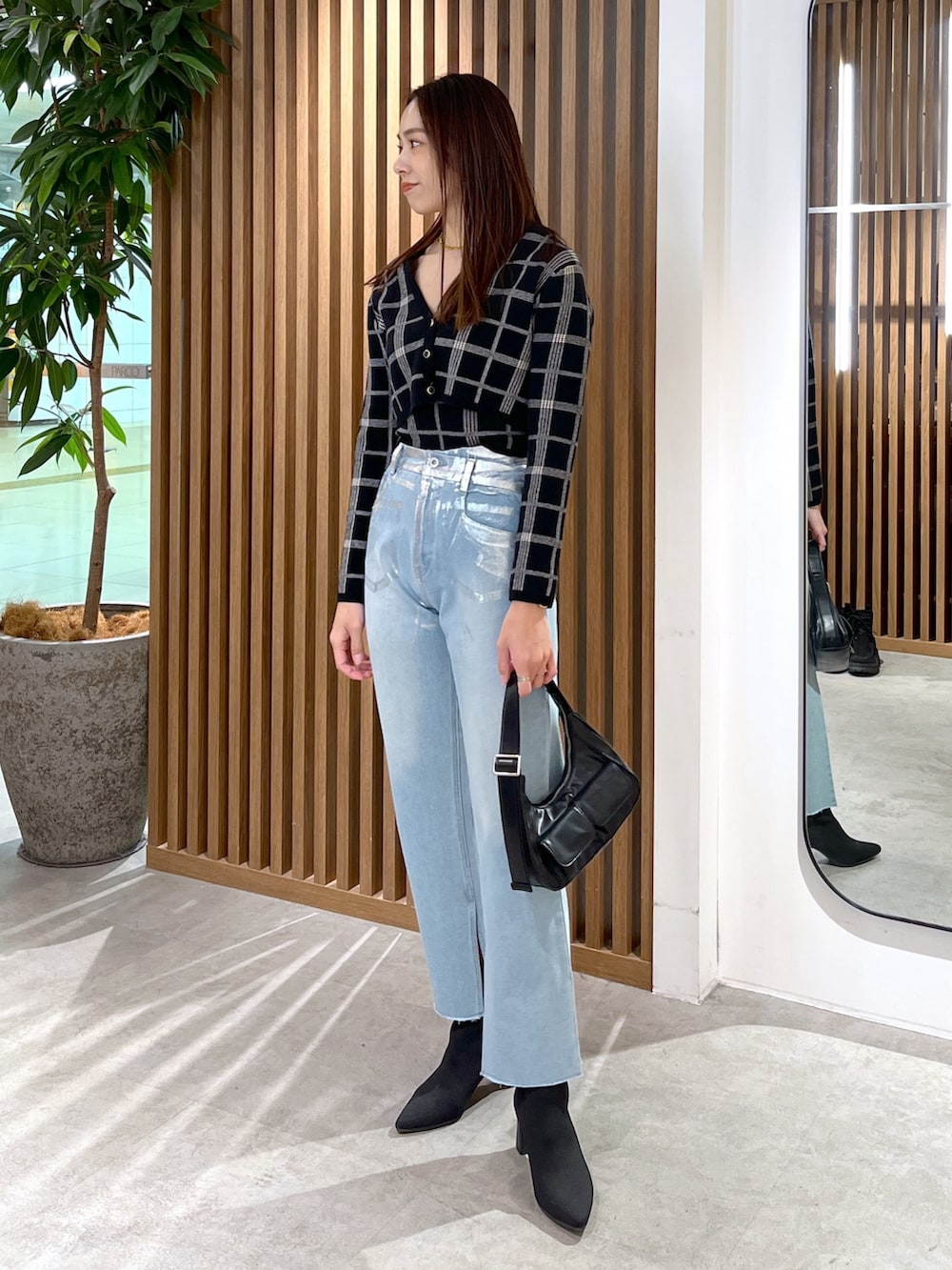 ブルー系のデニムパンツ、ブラック系のニット/セーター、ブラック系のショルダーバッグを着用したレディースの冬コーディネートの2枚目の写真