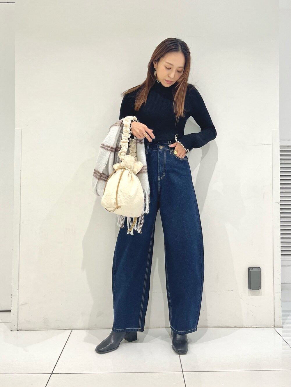 ブルー系のデニムパンツ、ブラック系のニット/セーター、ホワイト系のトートバッグを着用したレディースの冬コーディネートの2枚目の写真