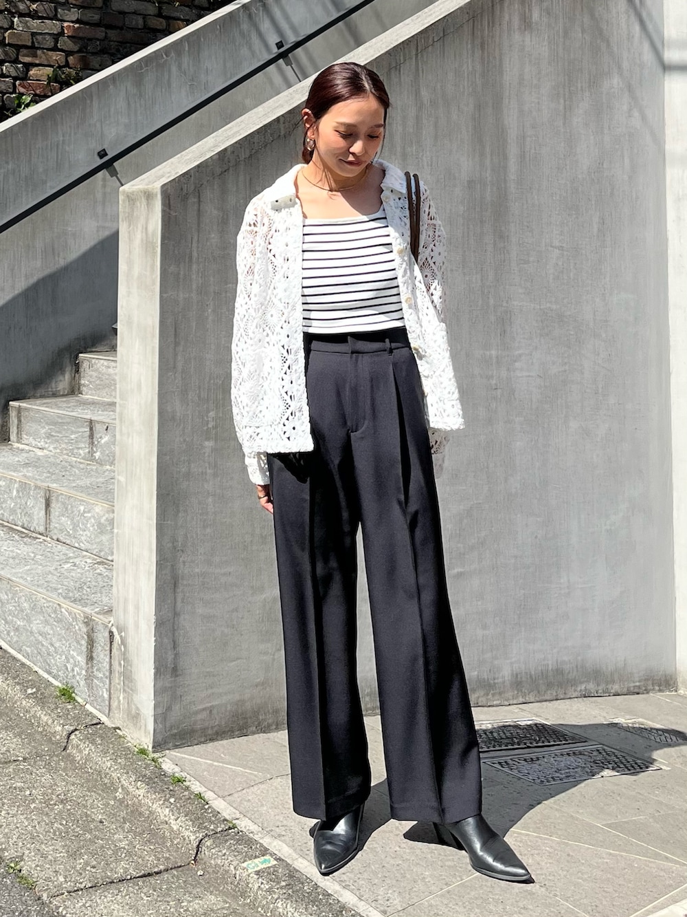 ブラック系のスラックス、ブラウン系のトートバッグ、ホワイト系のブルゾンを着用したレディースの春コーディネートの2枚目の写真