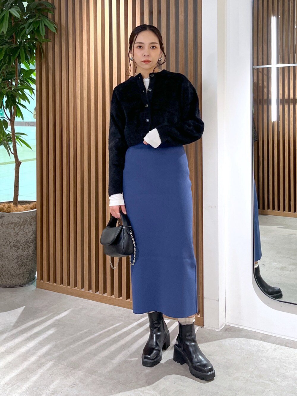 ブラック系のカーディガン/ボレロ、ブラック系のショルダーバッグ、ブルー系のスカートを着用したレディースの冬コーディネートの2枚目の写真