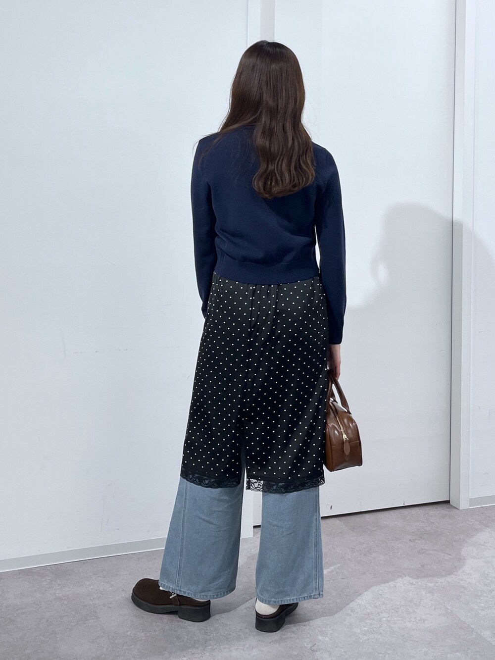 ブルー系のデニムパンツ、ブラウン系のハンドバッグ、ブラック系のスカートを着用したレディースの冬コーディネートの5枚目の写真