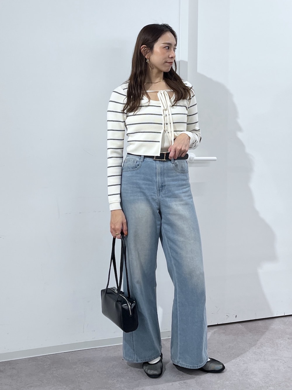 ブラック系のショルダーバッグ、ホワイト系のニット/セーター、ブルー系のデニムパンツを着用したレディースの冬コーディネートの4枚目の写真