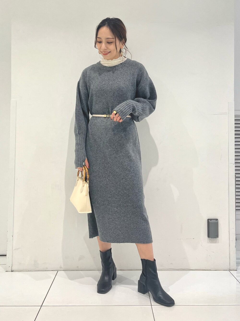 ホワイト系のショルダーバッグ、グレー系のワンピース、ブラック系のブーツを着用したレディースの冬コーディネートの2枚目の写真