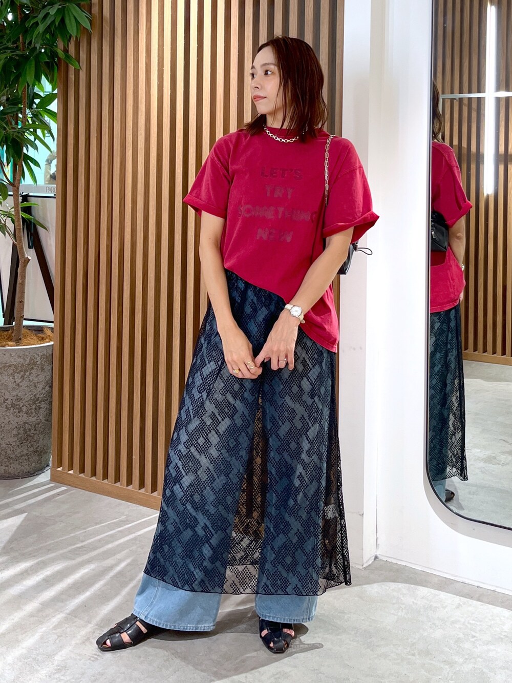 レッド系のTシャツ/カットソー、ブラック系のハンドバッグ、ブルー系のデニムパンツを着用したレディースの夏コーディネートの2枚目の写真