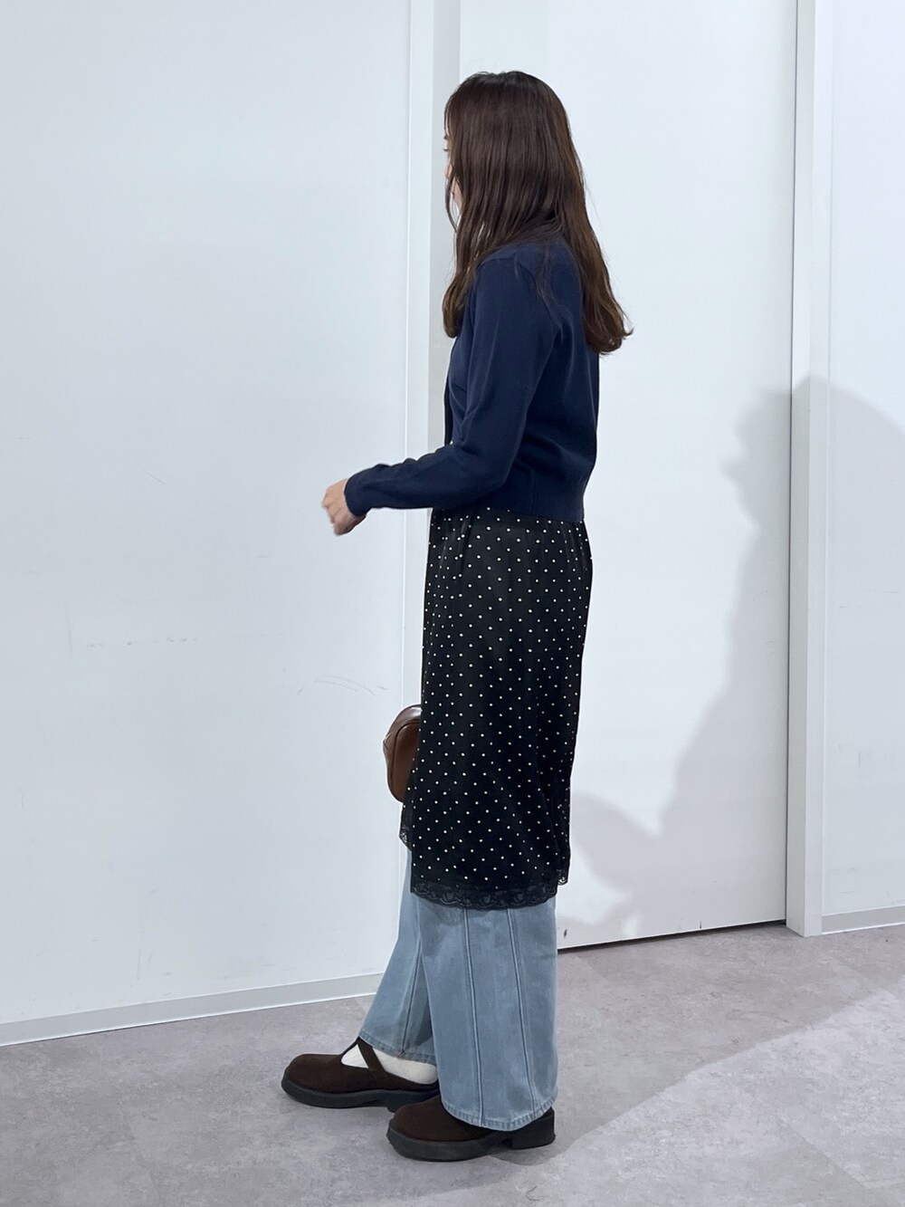 ブルー系のデニムパンツ、ブラウン系のハンドバッグ、ブラック系のスカートを着用したレディースの冬コーディネートの4枚目の写真