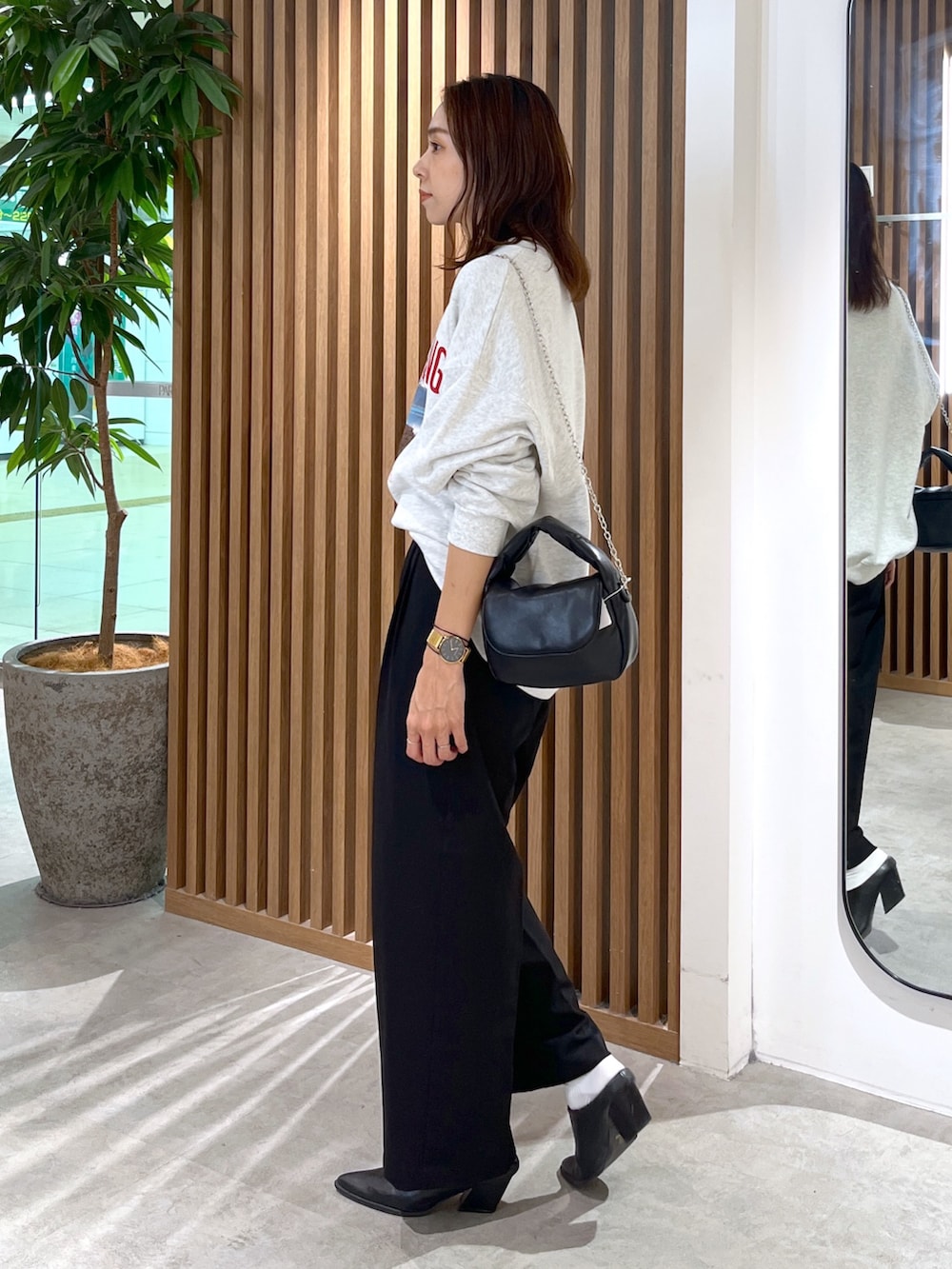 ホワイト系のスウェット、ブラック系のショルダーバッグ、ブラック系のスラックスを着用したレディースの秋コーディネートの4枚目の写真