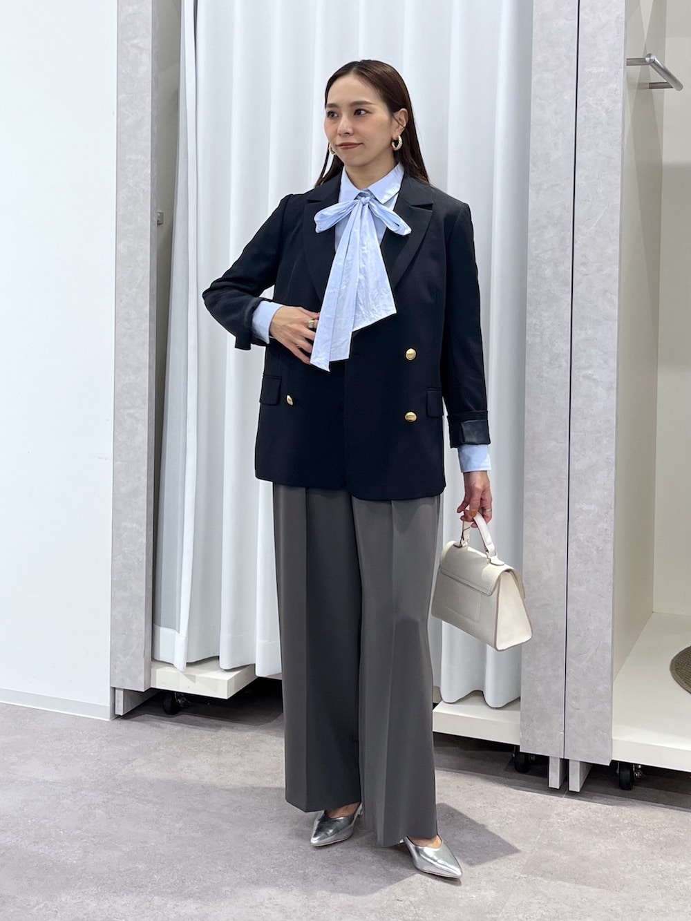 シルバー系のパンプス、グレー系のスラックス、ホワイト系のショルダーバッグを着用したレディースの冬コーディネートの2枚目の写真