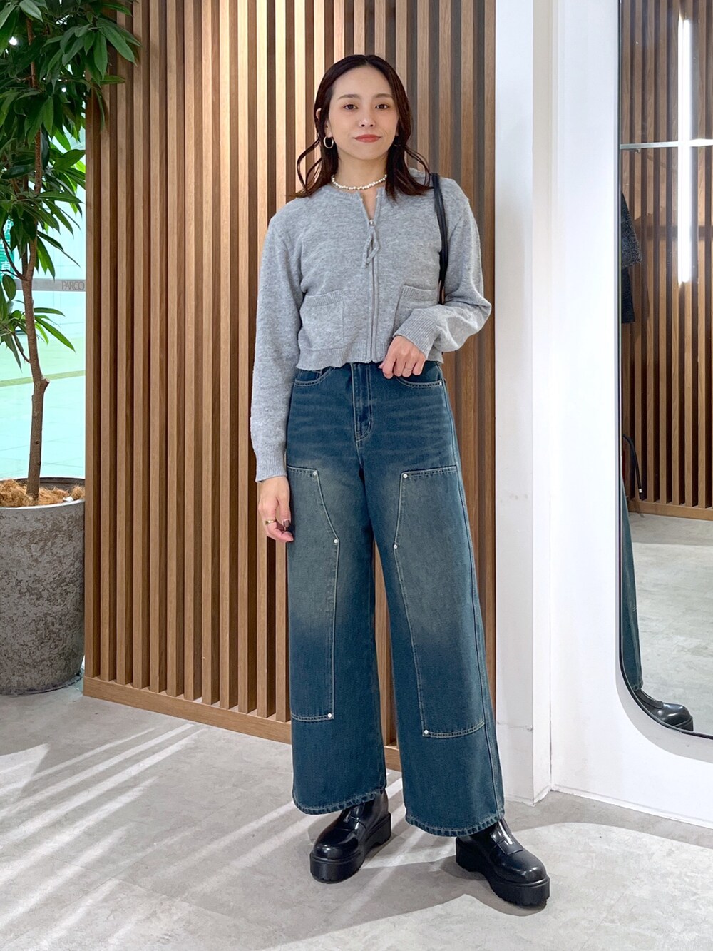 グレー系のワンピース、ブルー系のデニムパンツ、ブラック系のブーツを着用したレディースの冬コーディネートの2枚目の写真