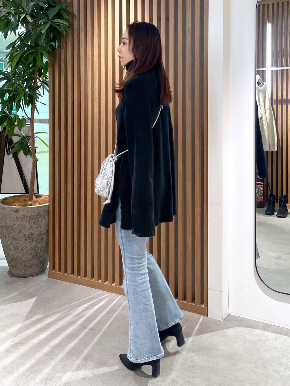 シルバー系のハンドバッグ、ブラック系のニット/セーター、ブルー系のデニムパンツを着用したレディースの冬コーディネートの3枚目の写真