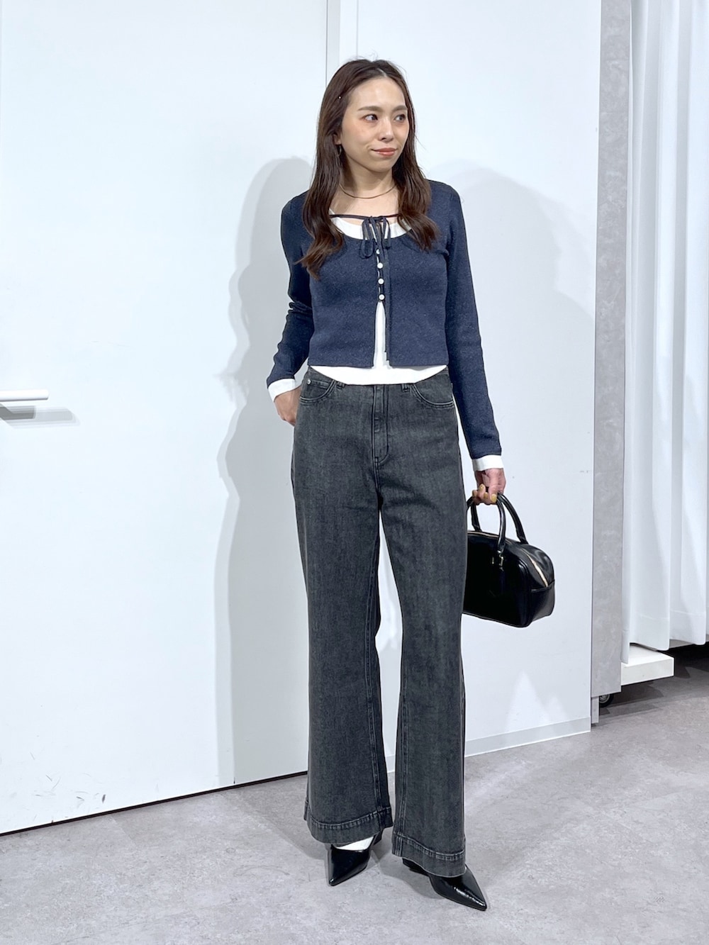 ブラック系のハンドバッグ、ブラック系のパンプス、ブラック系のデニムパンツを着用したレディースの春コーディネートの2枚目の写真