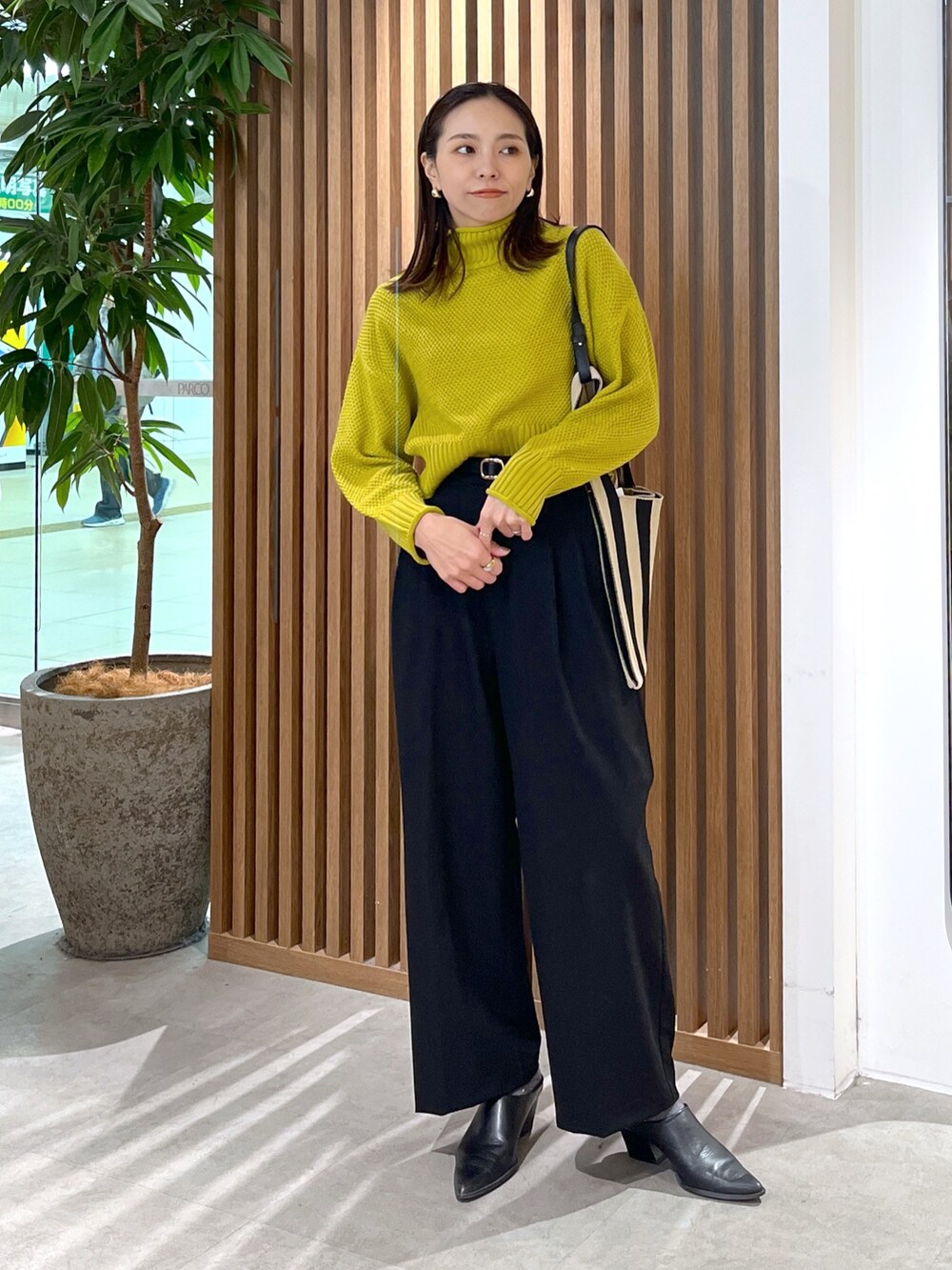 イエロー系のニット/セーター、ブラック系のスラックス、ブラック系のショルダーバッグを着用したレディースの冬コーディネートの8枚目の写真
