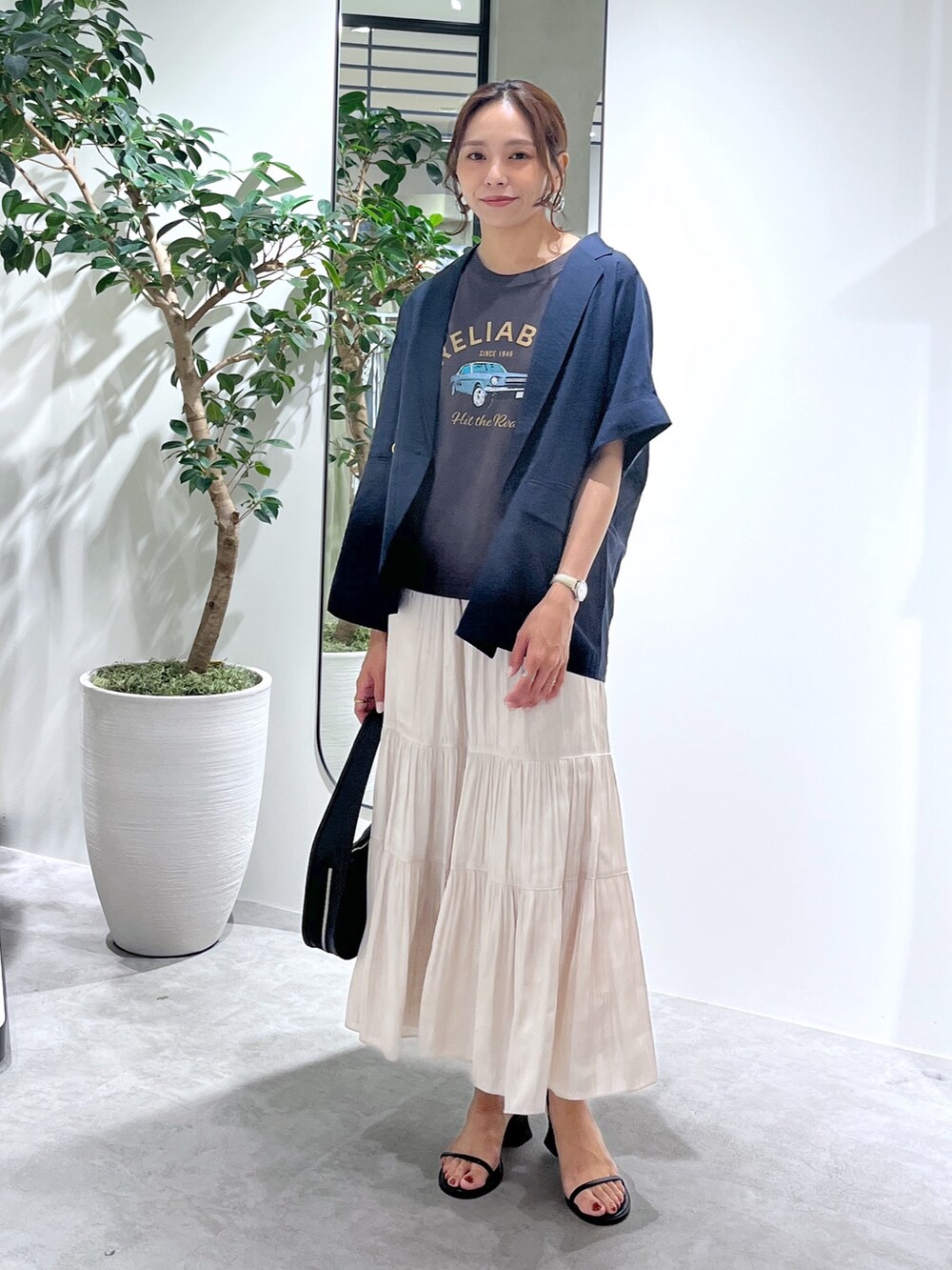 ブルー系のテーラードジャケット、ブラック系のハンドバッグ、ホワイト系のスカートを着用したレディースの夏コーディネートの2枚目の写真