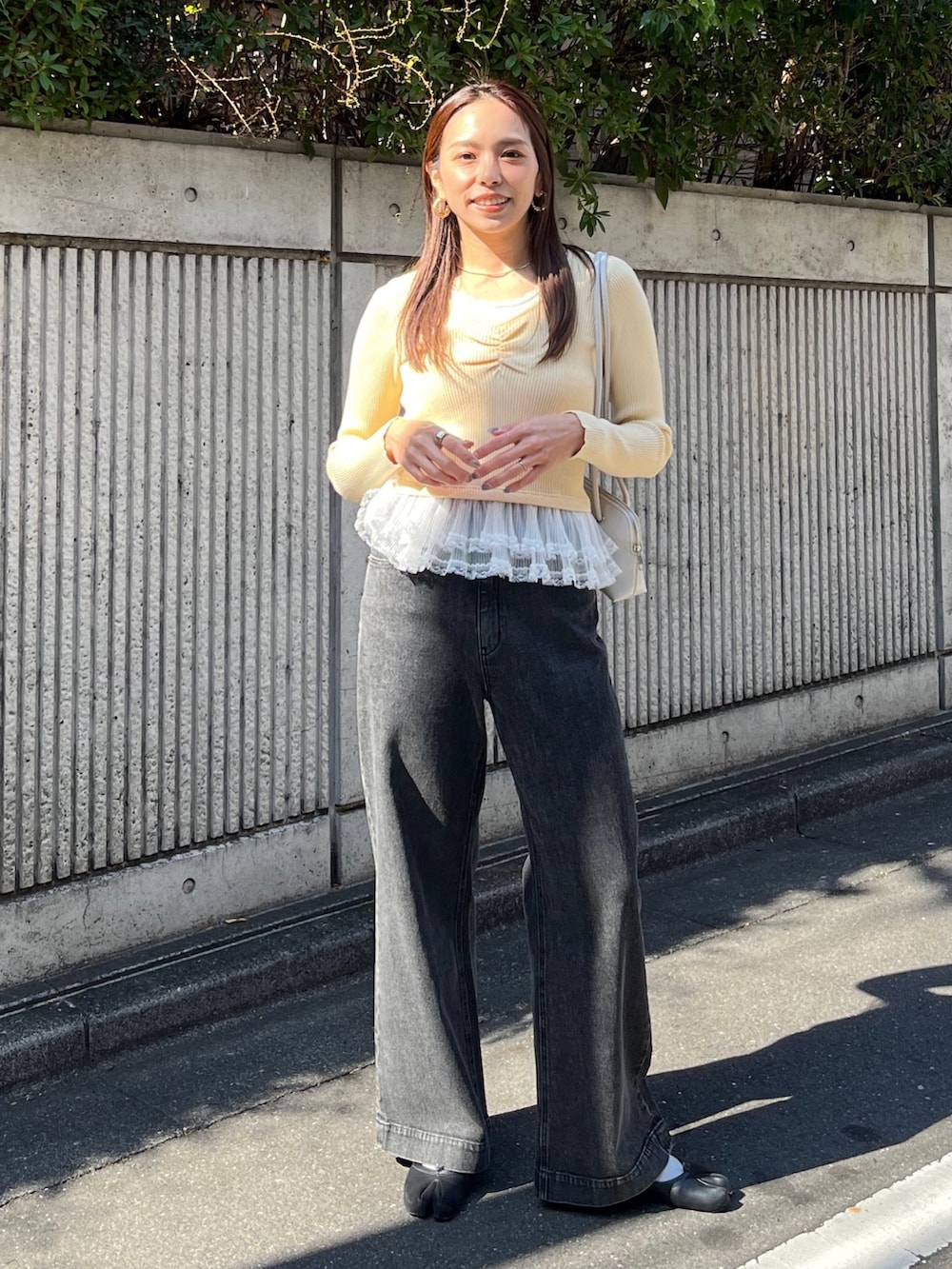 イエロー系のニット/セーター、ブラック系のデニムパンツ、ホワイト系のショルダーバッグを着用したレディースの冬コーディネートの2枚目の写真