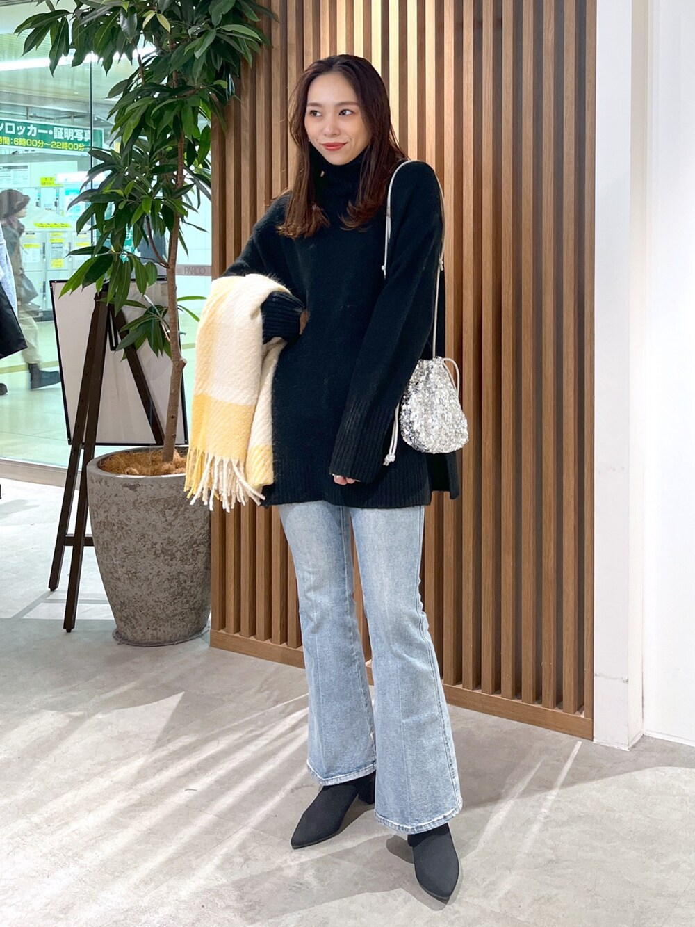 シルバー系のハンドバッグ、ブラック系のニット/セーター、ブルー系のデニムパンツを着用したレディースの冬コーディネートの2枚目の写真