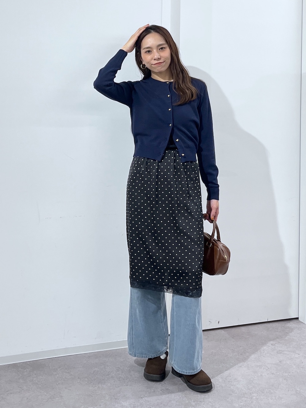 ブルー系のデニムパンツ、ブラウン系のハンドバッグ、ブラック系のスカートを着用したレディースの冬コーディネートの2枚目の写真