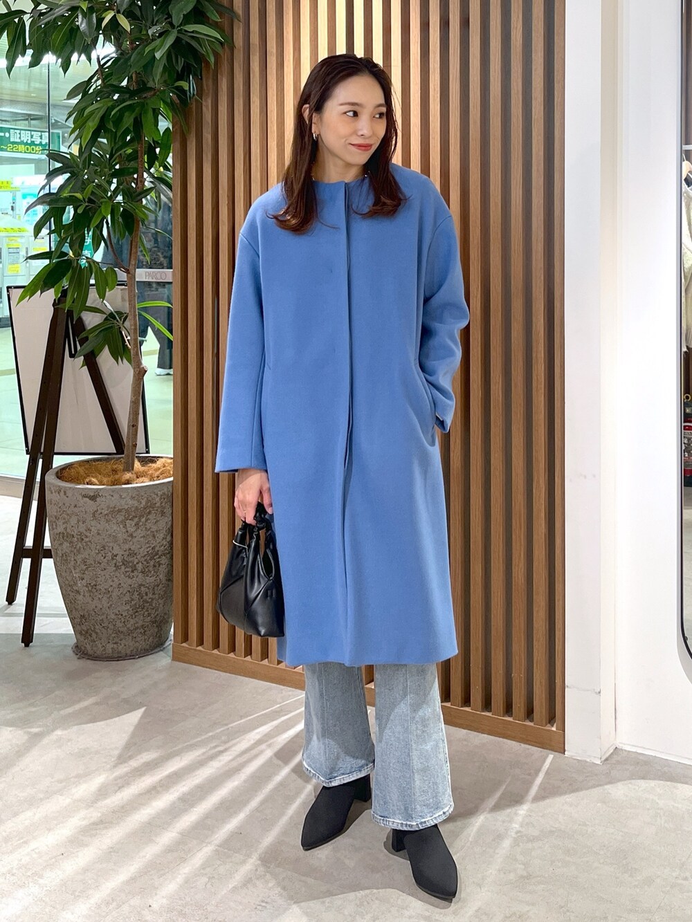 ブルー系のノーカラーコート、ホワイト系のニット/セーター、ブルー系のデニムパンツを着用したレディースの冬コーディネートの6枚目の写真