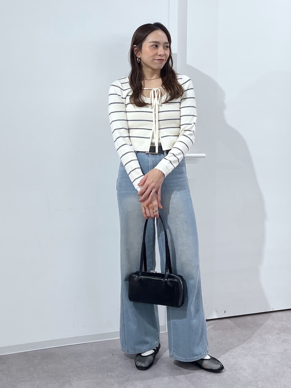 ブラック系のショルダーバッグ、ホワイト系のニット/セーター、ブルー系のデニムパンツを着用したレディースの冬コーディネートの9枚目の写真