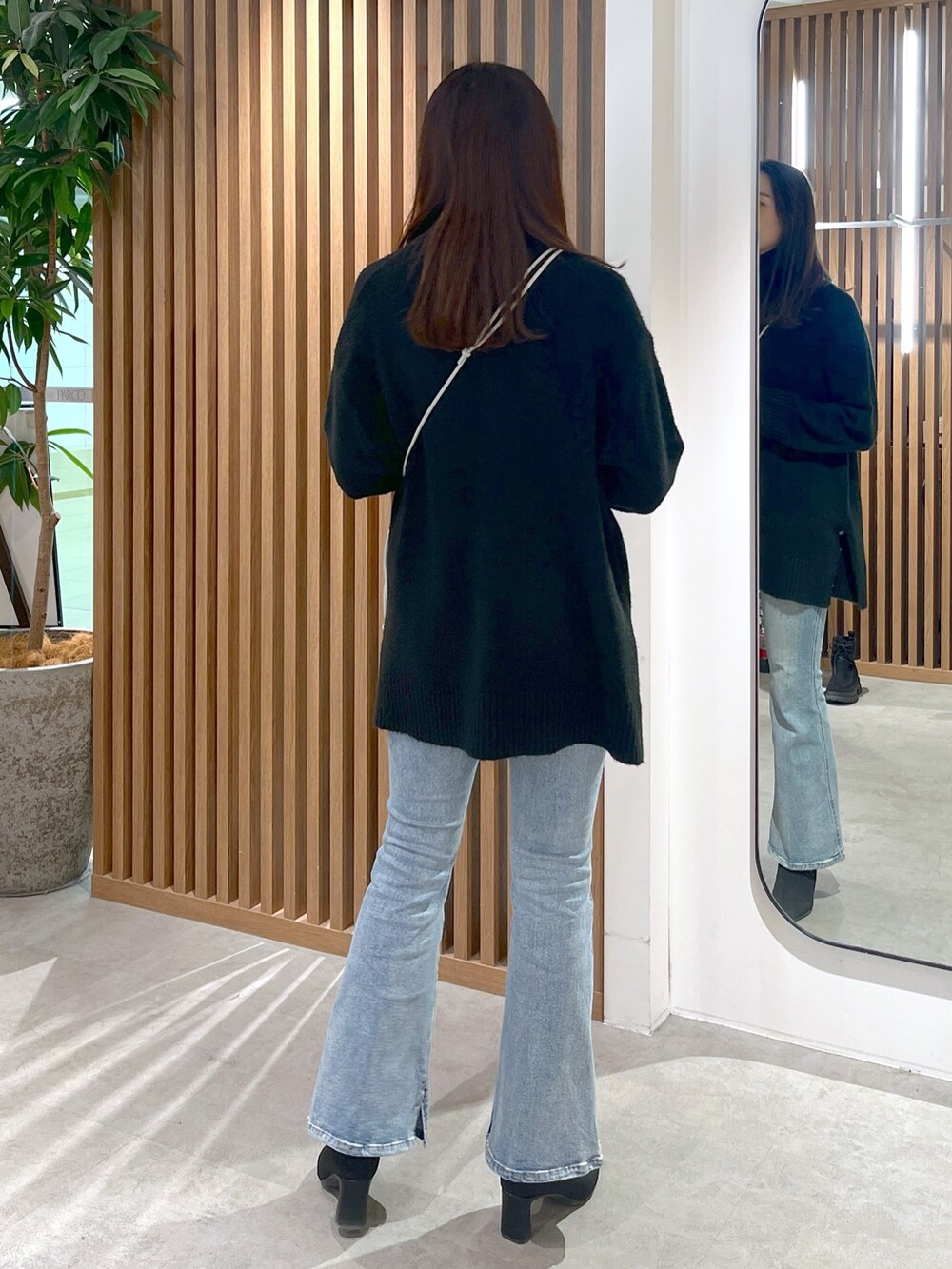 シルバー系のハンドバッグ、ブラック系のニット/セーター、ブルー系のデニムパンツを着用したレディースの冬コーディネートの4枚目の写真