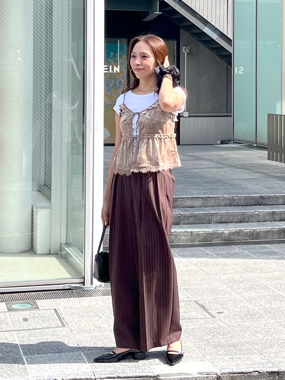 ブラック系のハンドバッグ、ブラック系のパンプス、ホワイト系のTシャツ/カットソーを着用したレディースの夏コーディネートの2枚目の写真