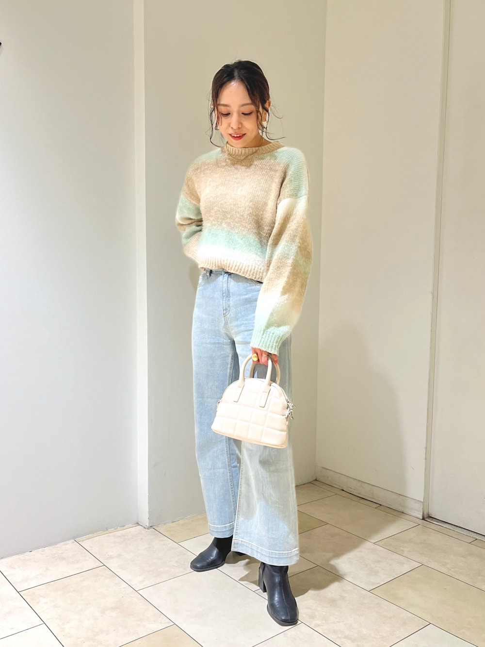 ホワイト系のデニムパンツ、グリーン系のニット/セーター、ホワイト系のハンドバッグを着用したレディースの冬コーディネートの3枚目の写真