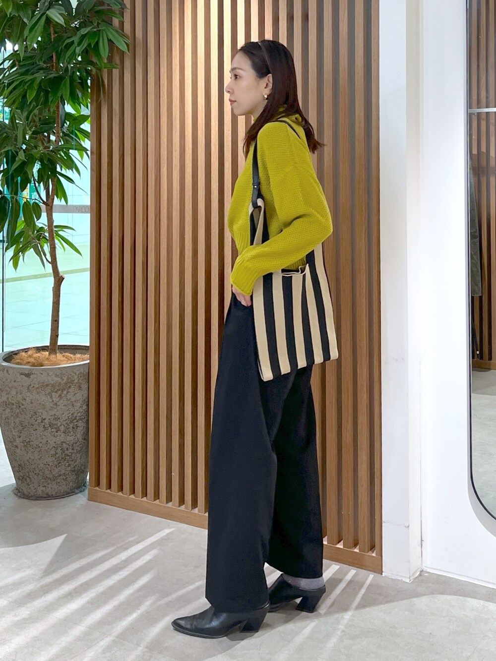 イエロー系のニット/セーター、ブラック系のスラックス、ブラック系のショルダーバッグを着用したレディースの冬コーディネートの4枚目の写真