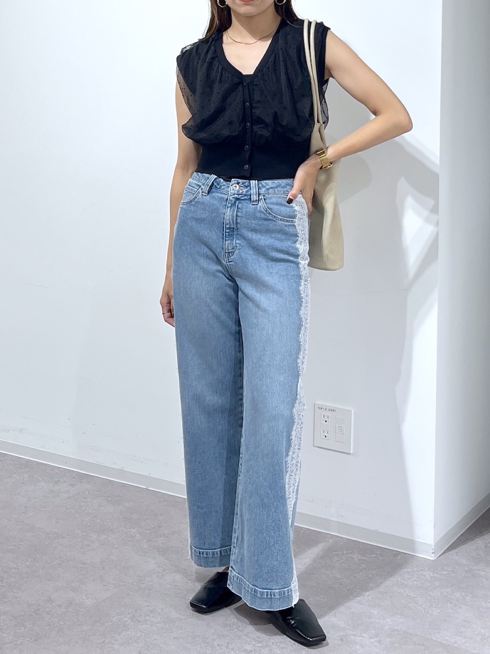 ブラック系のニット/セーター、ブルー系のデニムパンツ、ベージュ系のトートバッグを着用したレディースの夏コーディネートの3枚目の写真