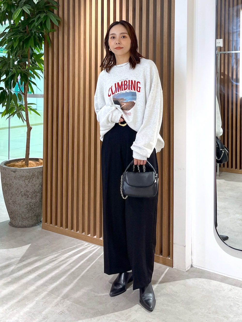 ホワイト系のスウェット、ブラック系のショルダーバッグ、ブラック系のスラックスを着用したレディースの秋コーディネートの2枚目の写真