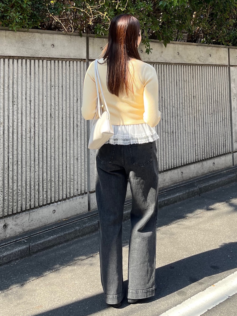 イエロー系のニット/セーター、ブラック系のデニムパンツ、ホワイト系のショルダーバッグを着用したレディースの冬コーディネートの5枚目の写真