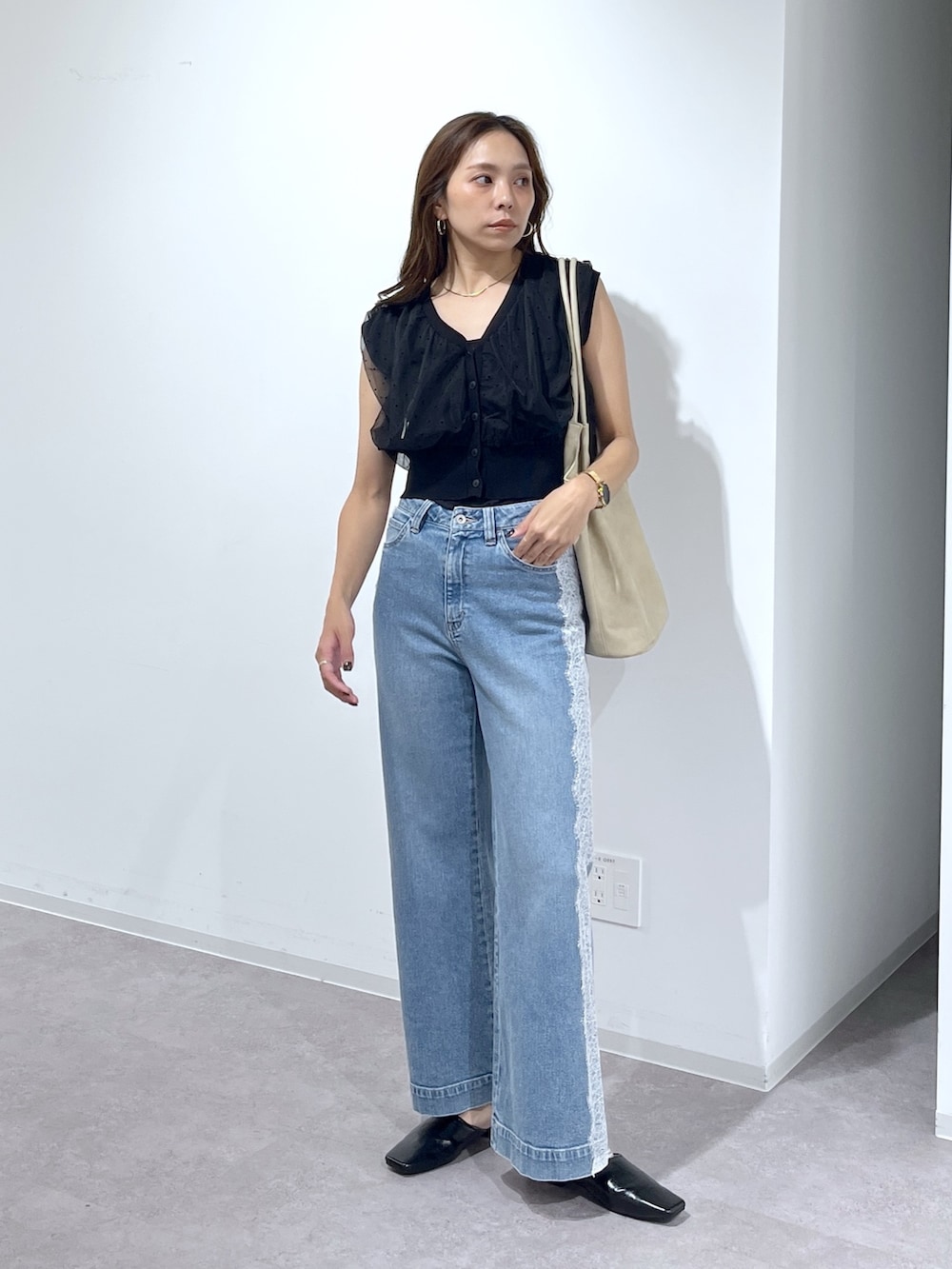 ブラック系のニット/セーター、ブルー系のデニムパンツ、ベージュ系のトートバッグを着用したレディースの夏コーディネートの2枚目の写真