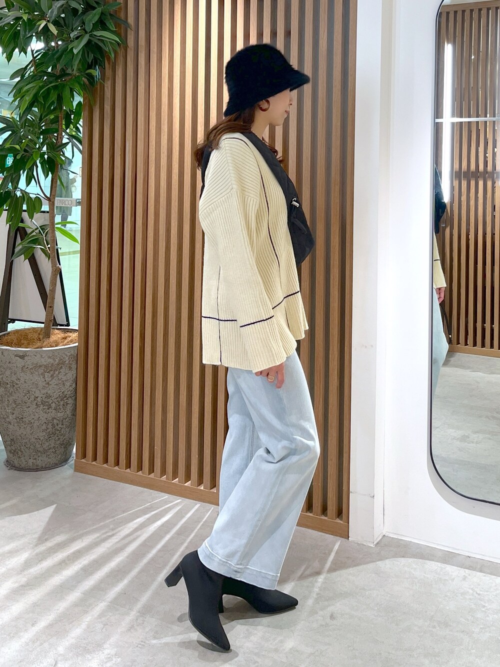 ブラック系のショルダーバッグ、ホワイト系のニット/セーター、ブルー系のデニムパンツを着用したレディースの冬コーディネートの4枚目の写真