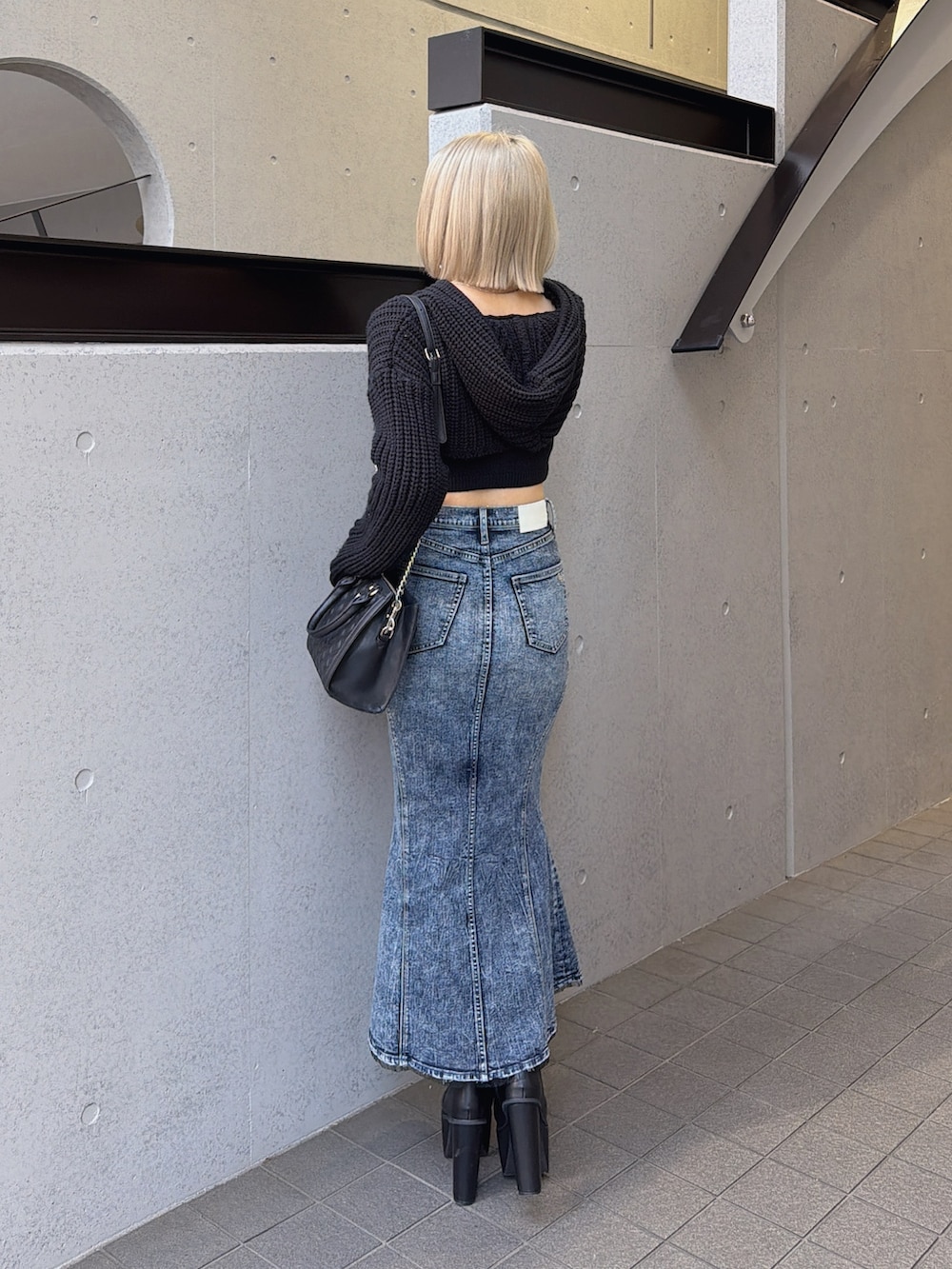 ブラック系のニット/セーター、ブルー系のデニムスカート、ブラック系のブーツを着用したレディースの冬コーディネートの2枚目の写真