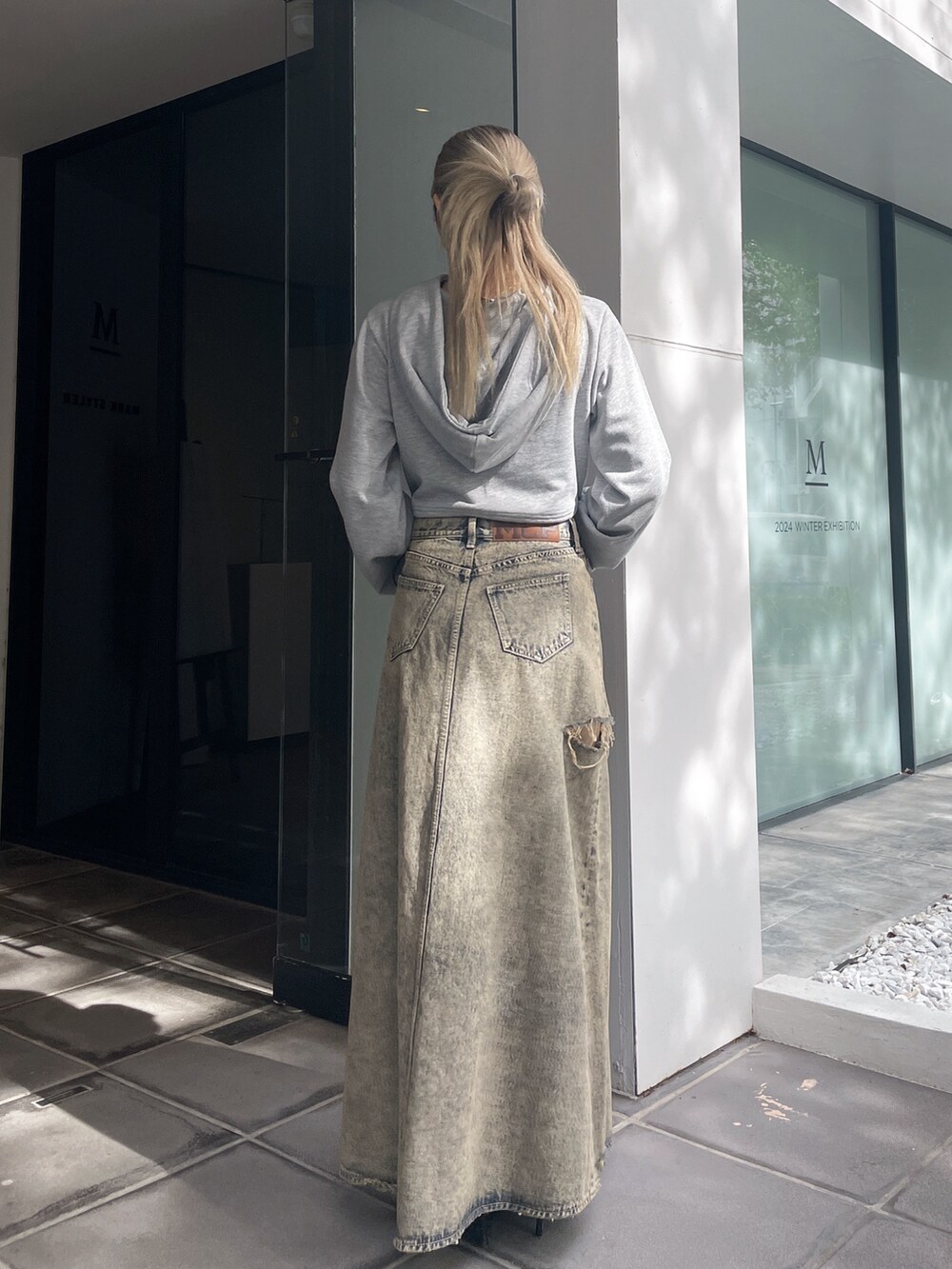 グレー系のパーカー、ブルー系のデニムスカート、ブラック系のパンプスを着用したレディースの秋コーディネートの2枚目の写真