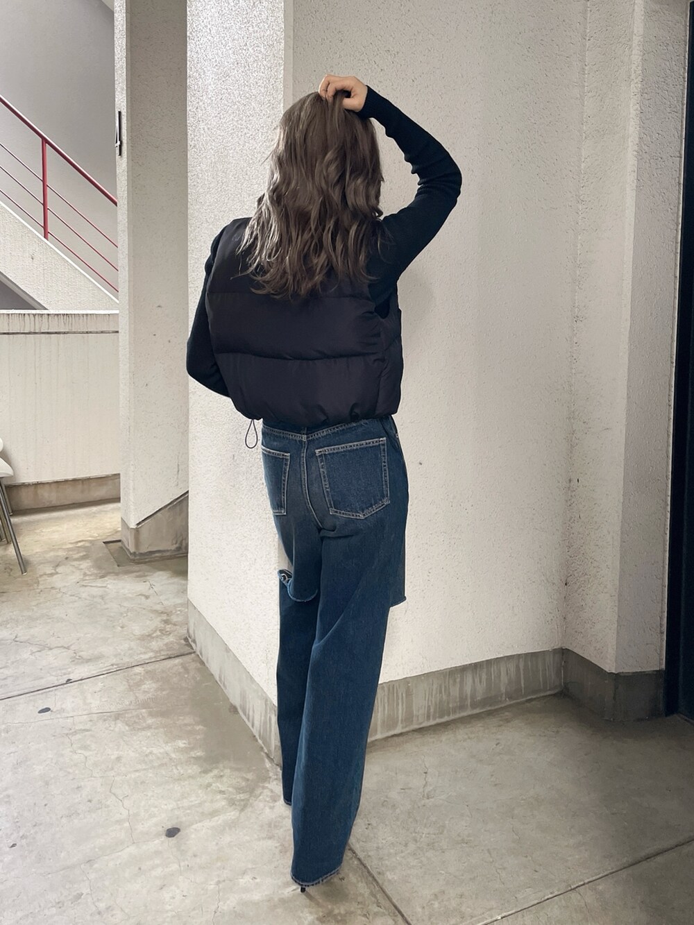 ブラック系のベスト、ブルー系のデニムパンツ、ブラック系のパンプスを着用したレディースの秋コーディネートの2枚目の写真