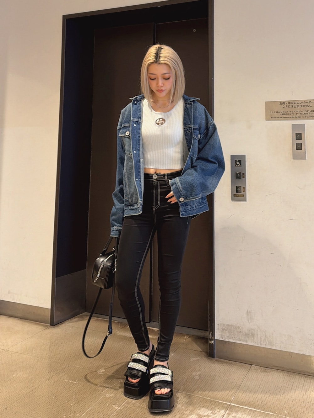 ブルー系のデニムジャケット、ブラック系のハンドバッグ、ブラック系のデニムパンツを着用したレディースの春コーディネートの2枚目の写真