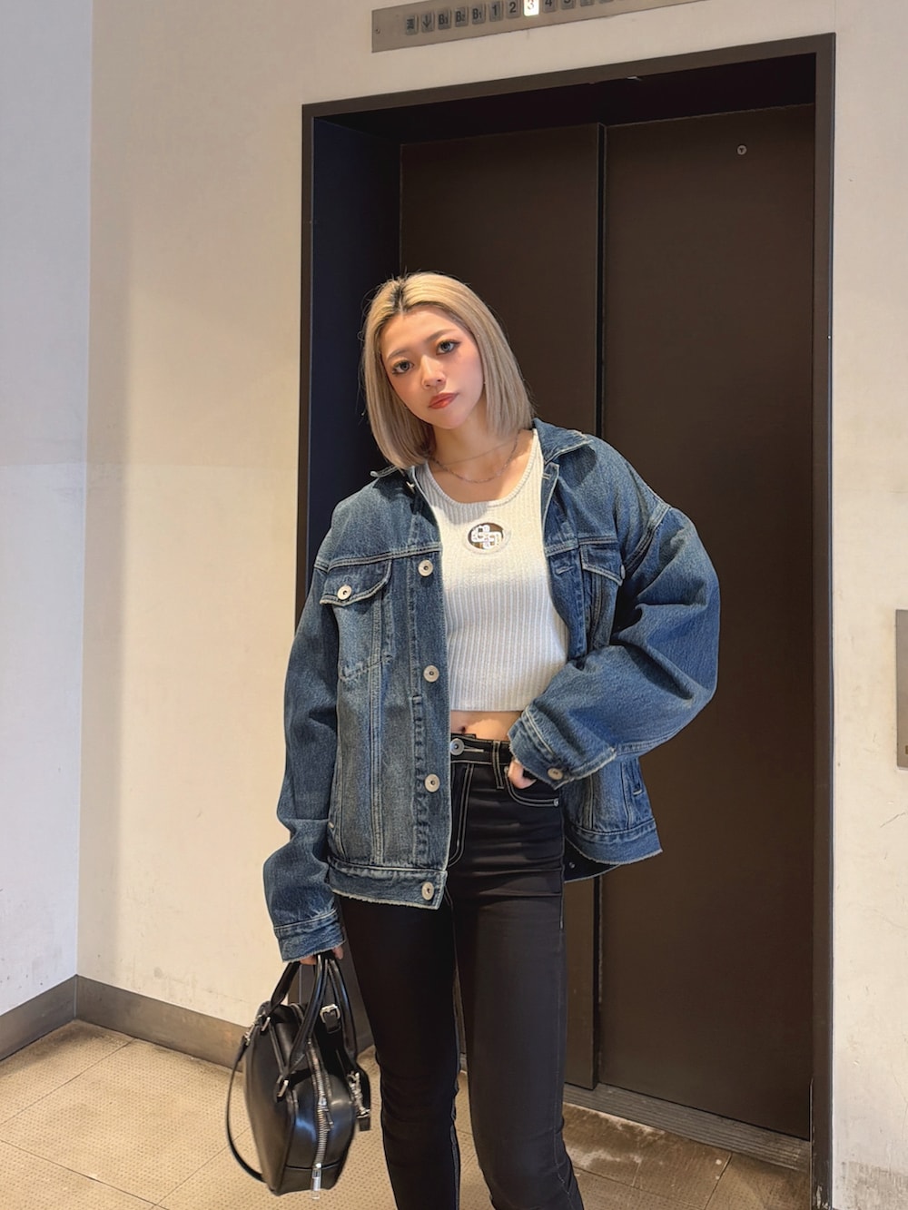 ブルー系のデニムジャケット、ブラック系のハンドバッグ、ブラック系のデニムパンツを着用したレディースの春コーディネートの3枚目の写真