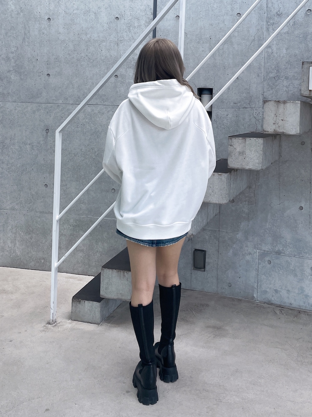 ホワイト系のパーカー、ブルー系のデニムスカート、ブラック系のブーツを着用したレディースの秋コーディネートの4枚目の写真