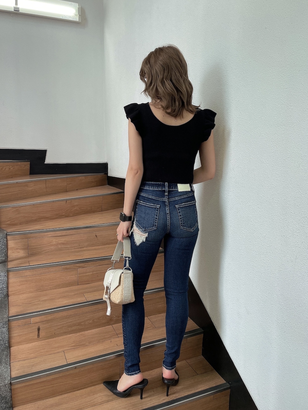 ブラック系のニット/セーター、ホワイト系のハンドバッグ、ブルー系のデニムパンツを着用したレディースの春コーディネートの2枚目の写真