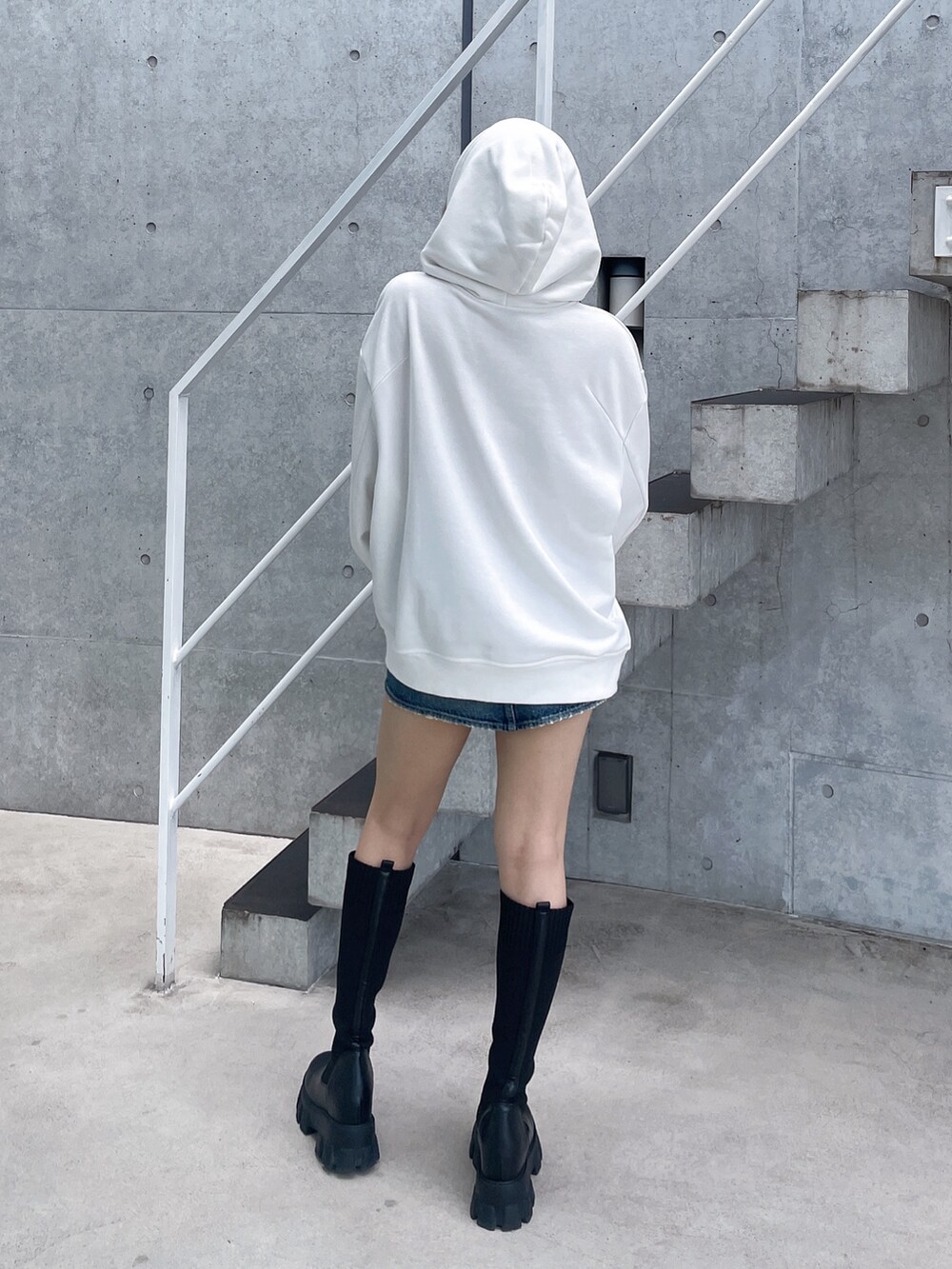 ホワイト系のパーカー、ブルー系のデニムスカート、ブラック系のブーツを着用したレディースの秋コーディネートの3枚目の写真