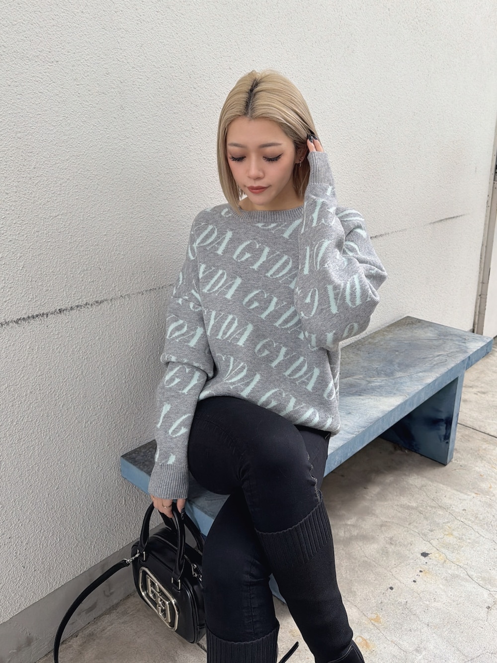 グレー系のニット/セーター、ブラック系のハンドバッグ、ブラック系のブーツを着用したレディースの春コーディネートの2枚目の写真