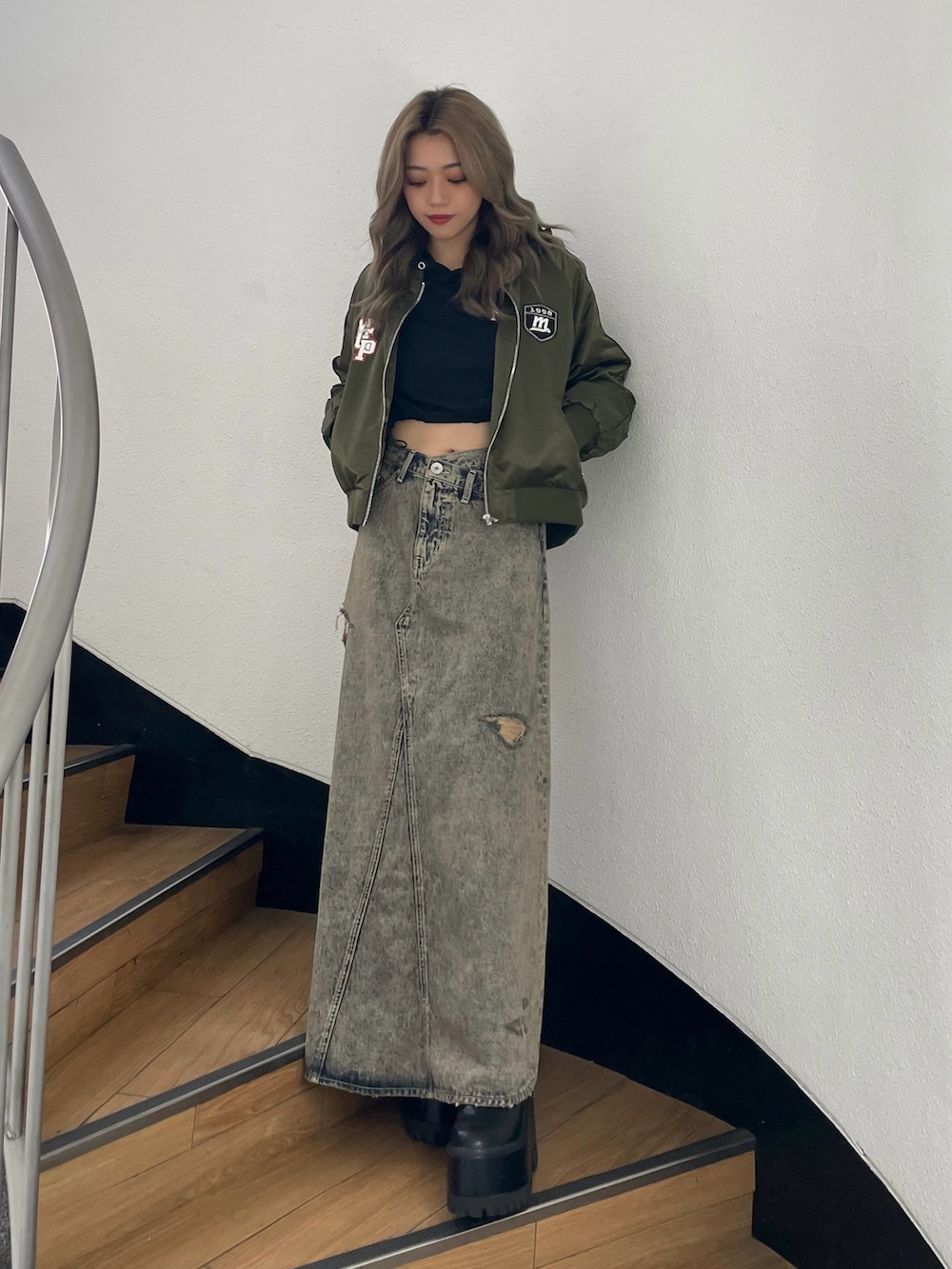 グリーン系のブルゾン、ブルー系のデニムスカート、ブラック系のブーツを着用したレディースの秋コーディネートの2枚目の写真