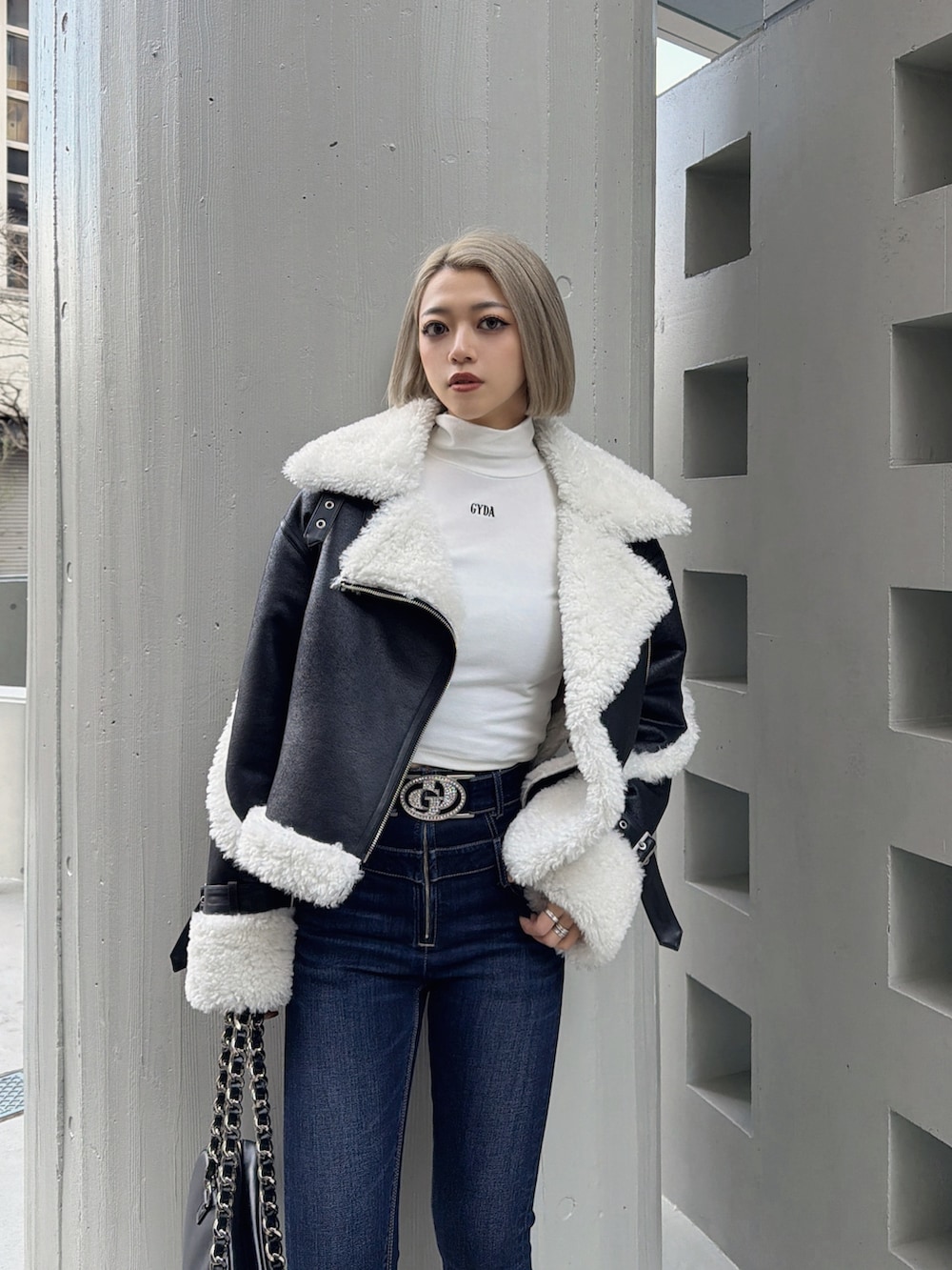 ブラック系のムートンコート、ホワイト系のTシャツ/カットソー、ブルー系のデニムパンツを着用したレディースの冬コーディネートの4枚目の写真